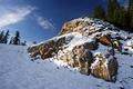 Morgensonnenbeleuchteter Felsen neben der Schipiste. Eine einsame Schispur und mehrere Fuspuren im Schnee.