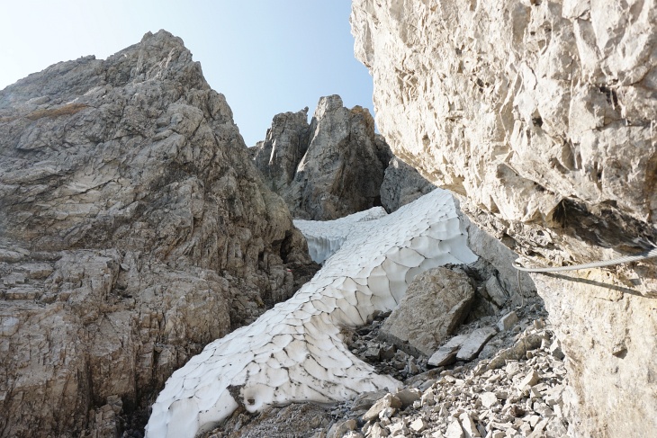 Die Schlucht mit dem Hartschneefeld schaut auf den ersten Blick gar nicht so schlimm aus. Aber links sind die Felsen durch das Schmelzwasser glitschig und rechts liefert kurz darauf eine kleine Steinlawine dem Steinhaufen Nachschub.