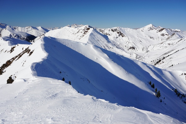 Abgefahren wird über einen Vorgipfel - ebenfalls mit Gipfelkreuz - im Steilhang beim Übergang vom Schatten zur Sonne